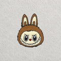 Brown Labubu embroidered patch displayed on a light grey felt background.