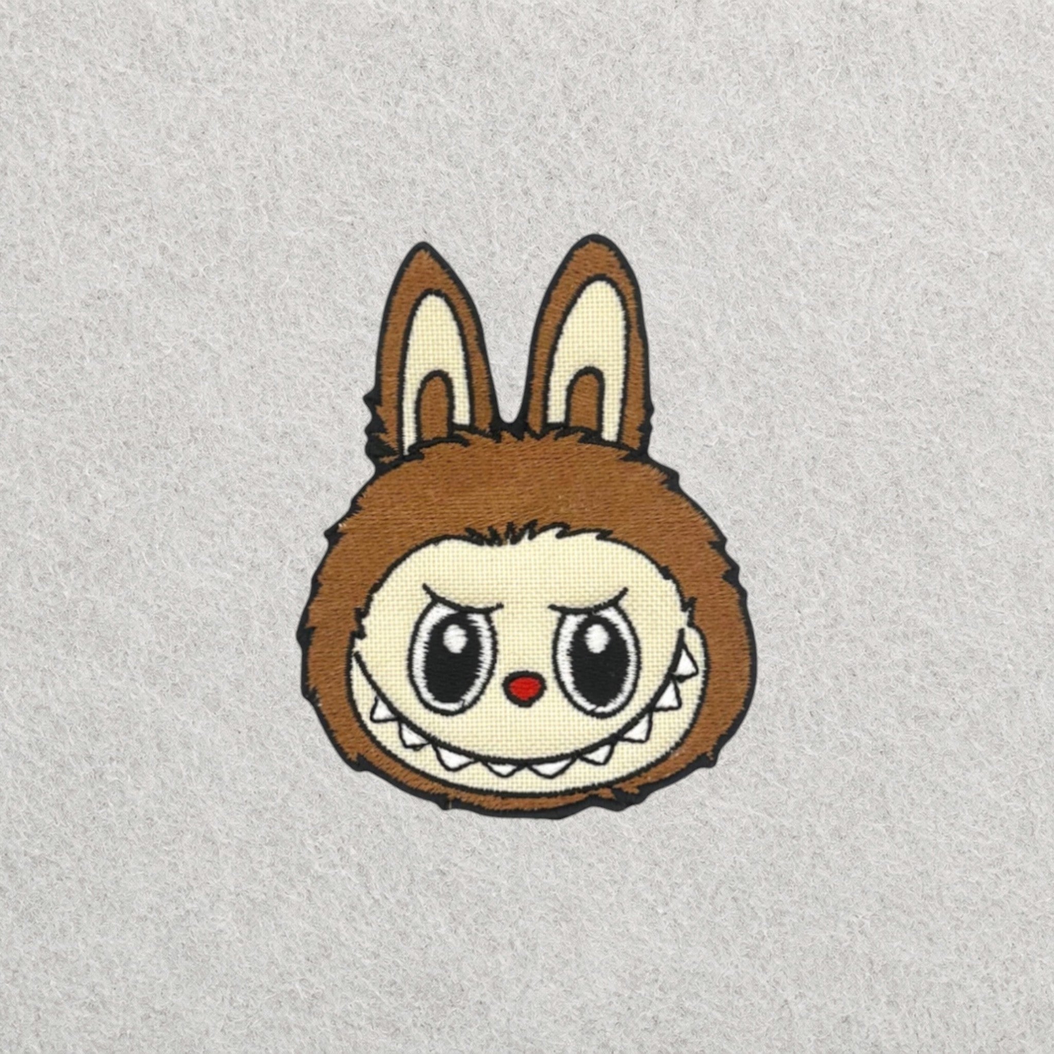 Brown Labubu embroidered patch displayed on a light grey felt background.