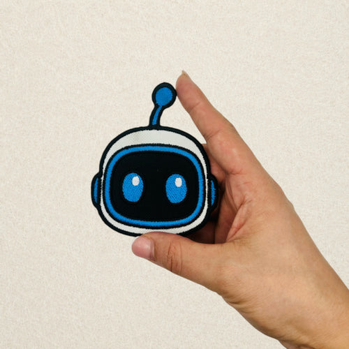 Astro Bot Head embroidered patch shown in hand to demonstrate its actual size.