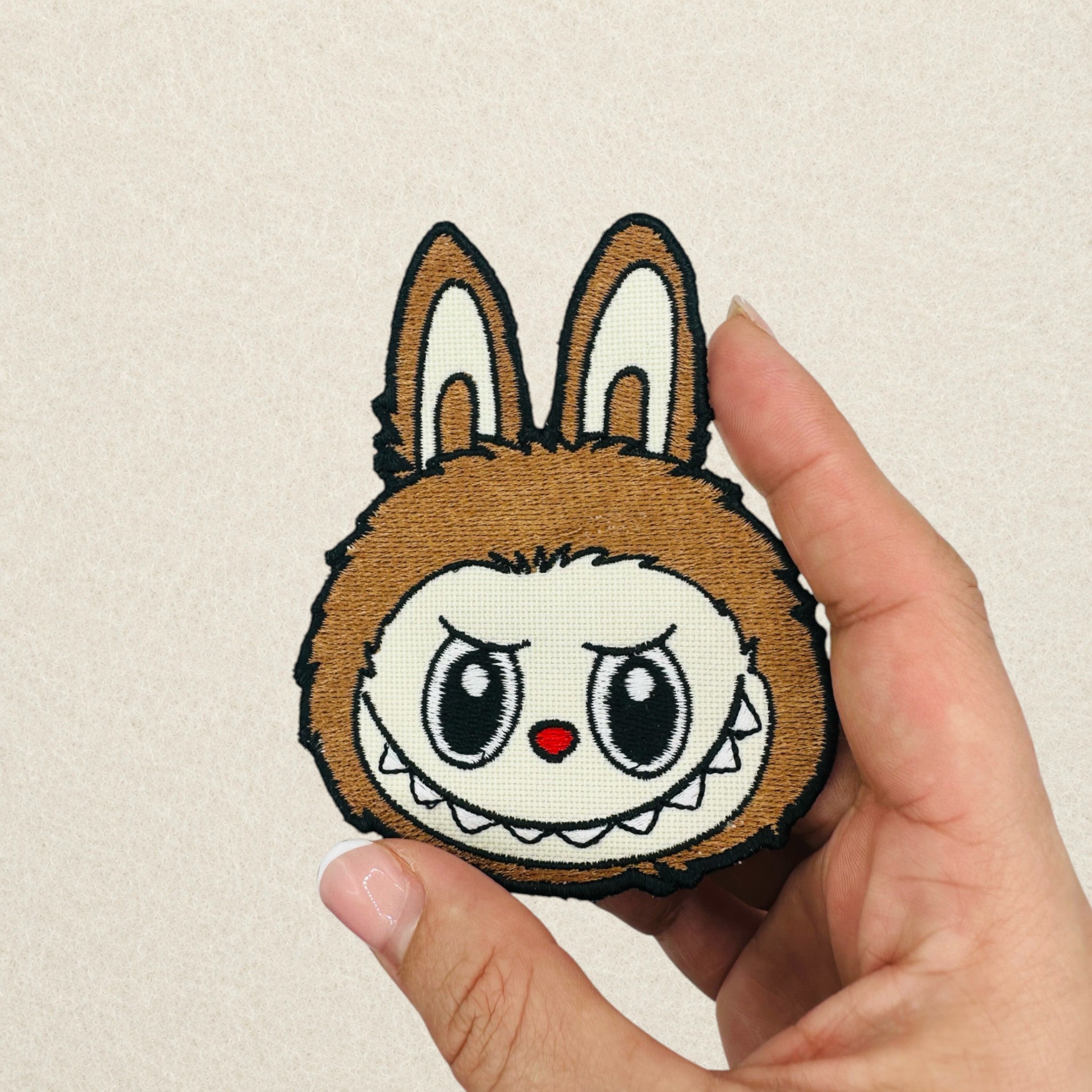 Brown Labubu embroidered patch shown in hand to demonstrate its actual size.