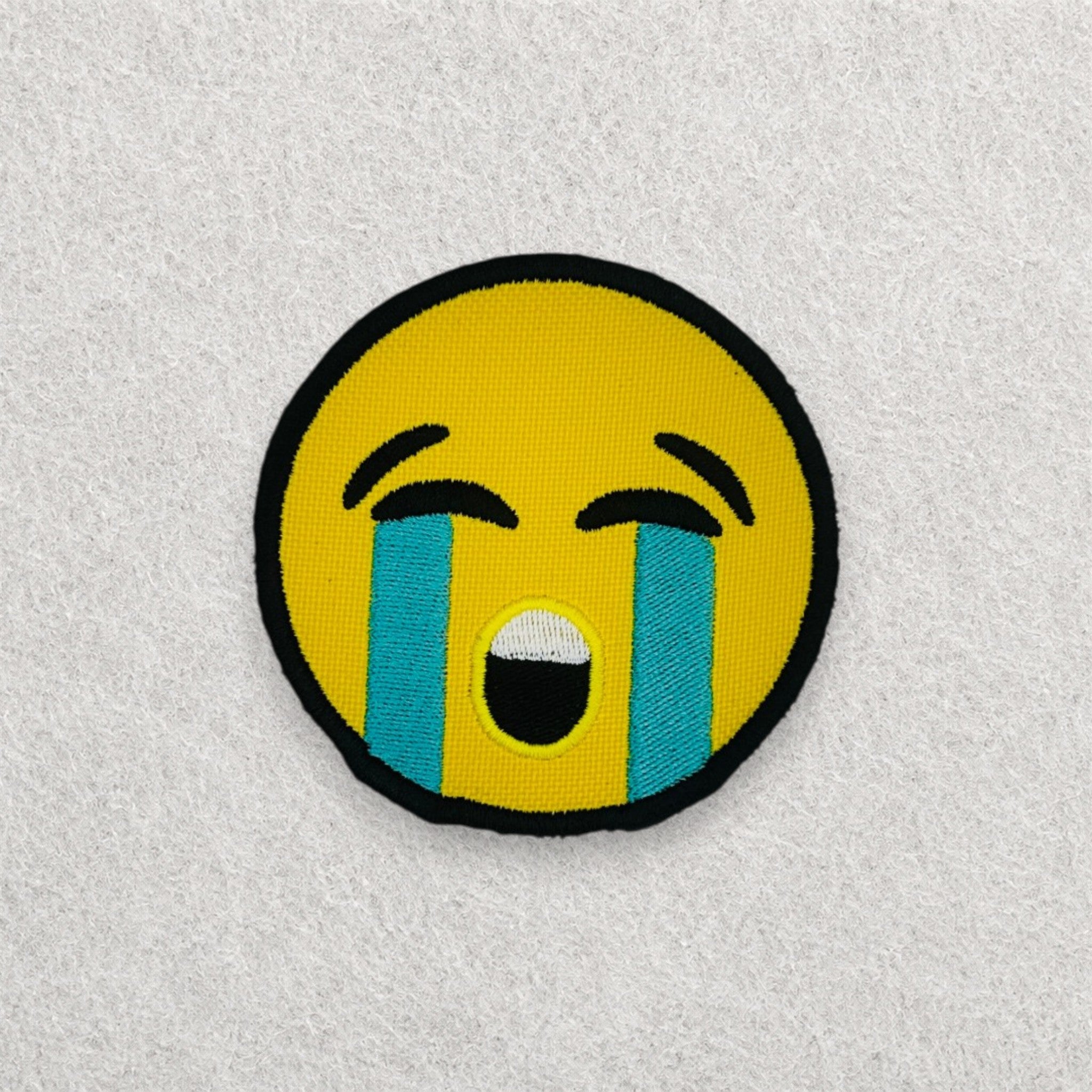 Crying Face Emoji embroidered patch displayed on a light grey felt background.