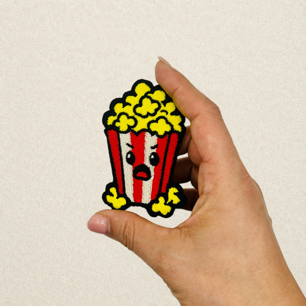 Grumpy Popcorn embroidered patch shown in hand to demonstrate its actual size.