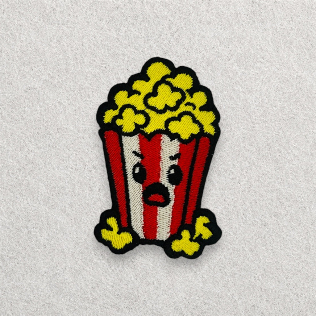 Grumpy Popcorn embroidered patch displayed on a light grey felt background.