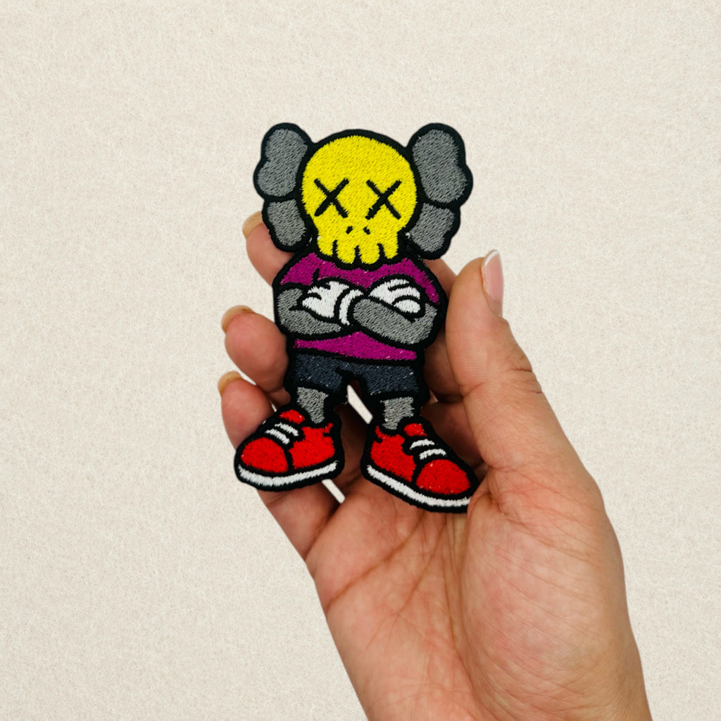 KAWS Companion embroidered patch shown in hand to demonstrate its actual size.