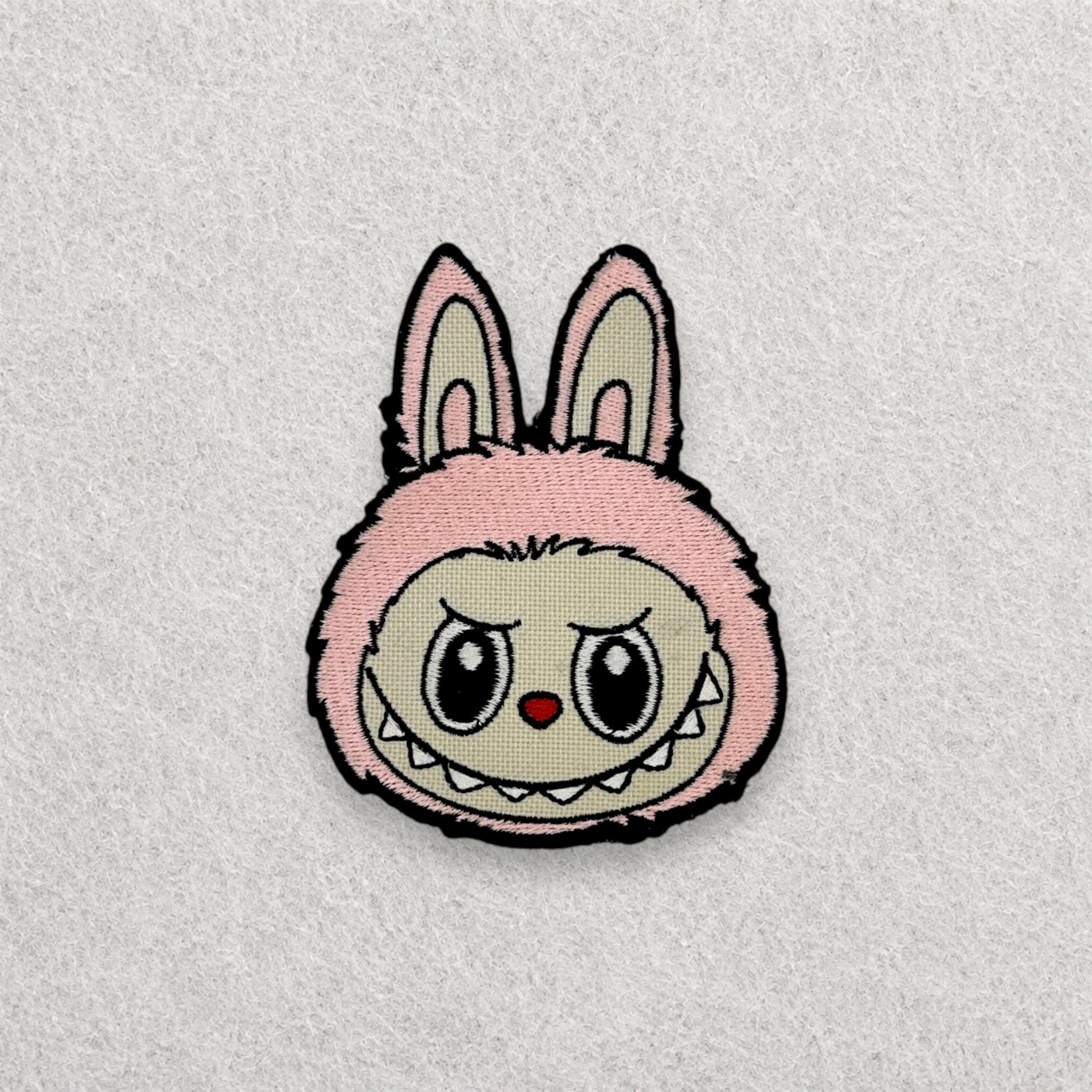 Pink Labubu embroidered patch displayed on a light grey felt background.