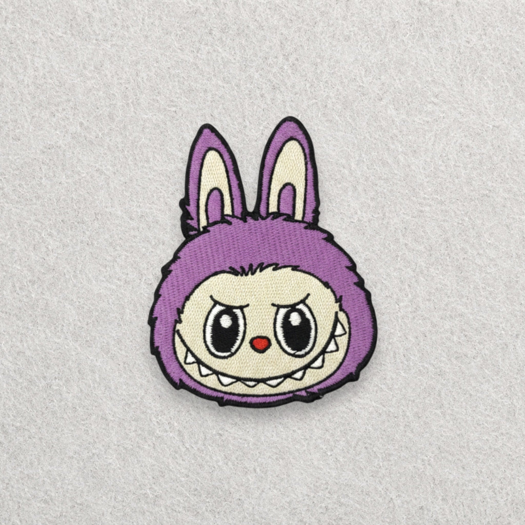 purple Labubu embroidered patch displayed on a light grey felt background.