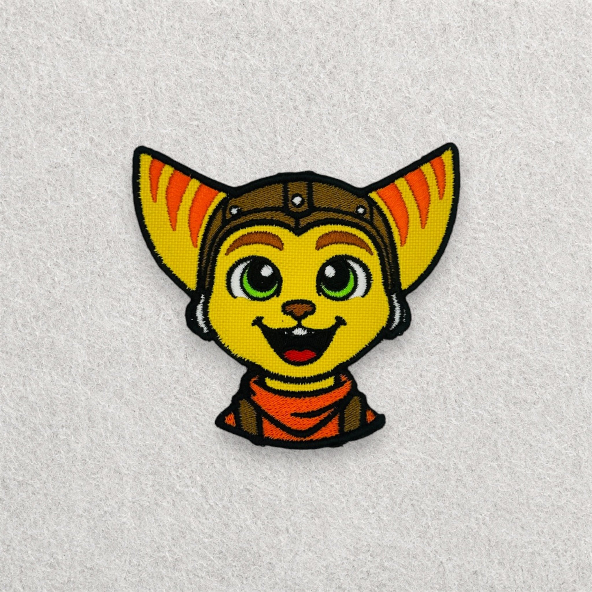 Ratchet inspired embroidered patch displayed on a light grey felt background.