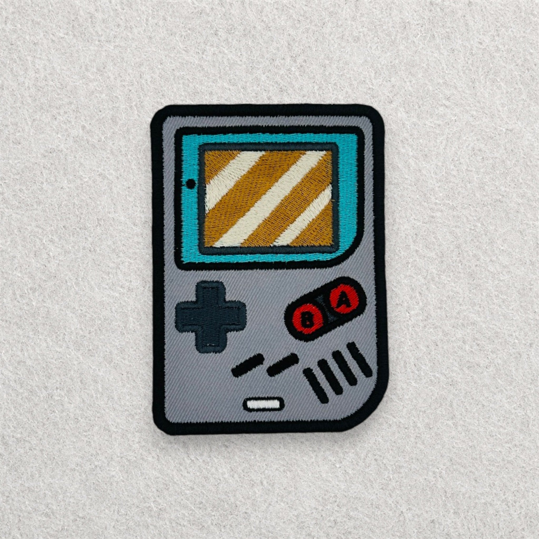 Retro Game Boy inspired embroidered patch displayed on a light grey felt background.