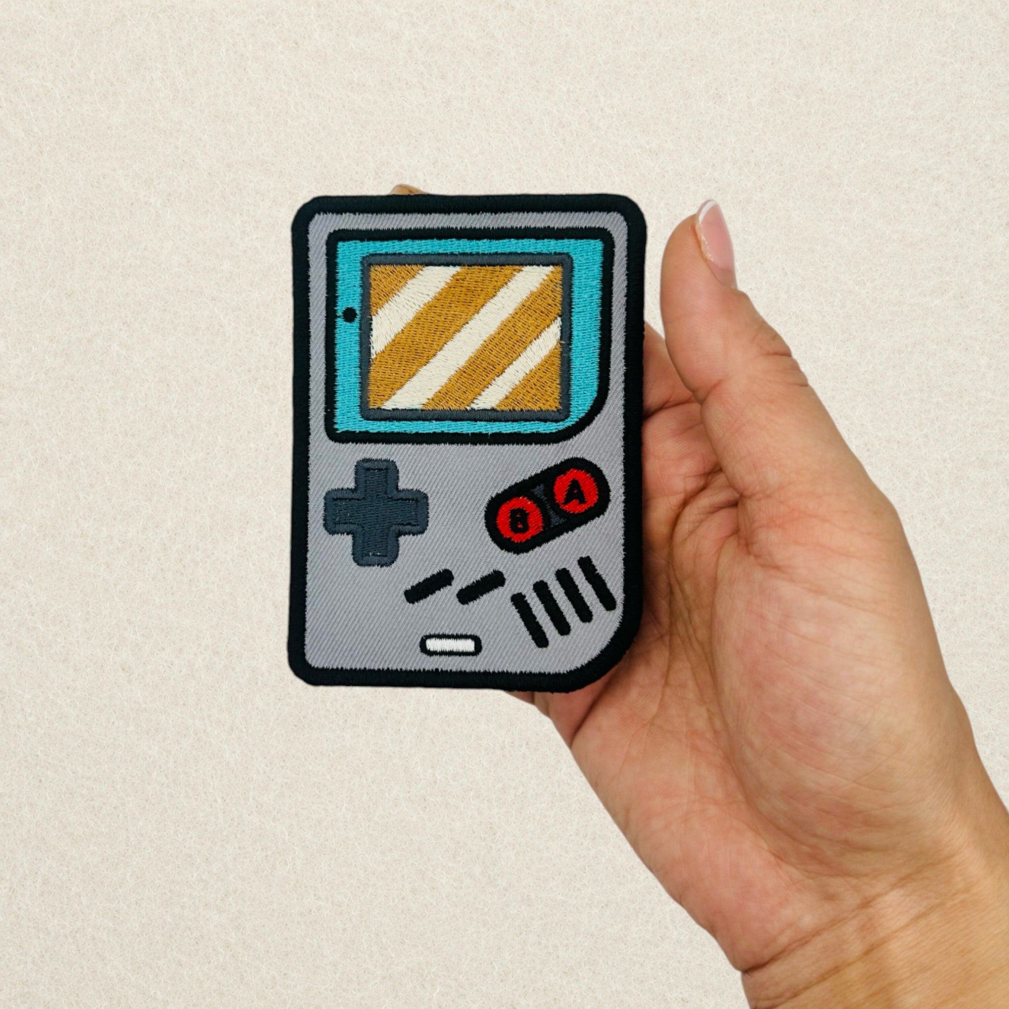 Retro Game Boy inspired embroidered patch shown in hand to demonstrate its actual size.