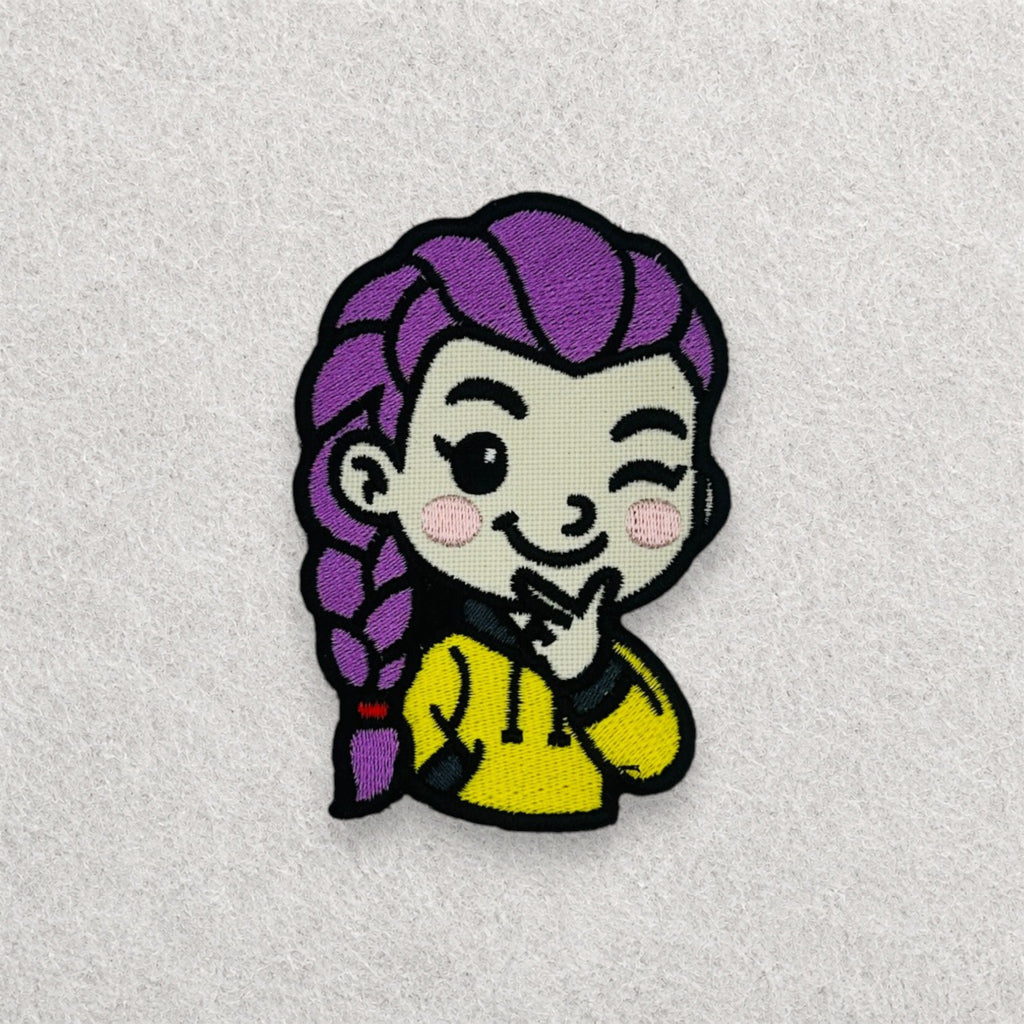 Rumi K-pop inspired embroidered patch featuring a cute winking character with purple braided hair and a yellow hoodie, finished with detailed stitching and a black embroidered border.