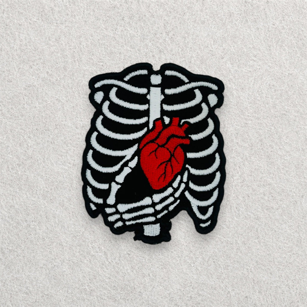 Skeleton Heart embroidered patch displayed on a light grey felt background.